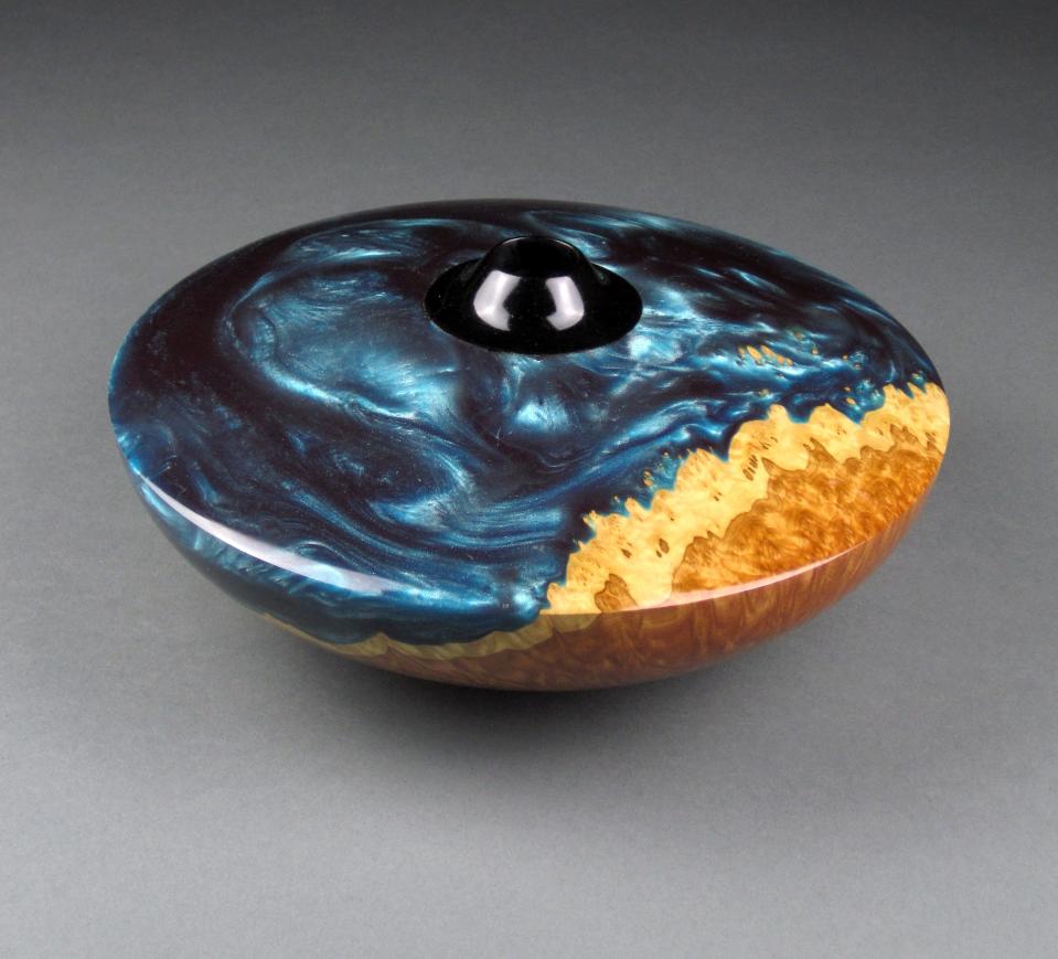 Milford artist Jon Berke uses a combination of a resin, dyed ocean blue with a silver powder combined with an Australian Brown Mallee burl wood then turned on lathe turned into a hollow vessel with a finish of between 15 to 20 coats of a hand rubbed wipe on polyurethane to achieve a glass like finish.