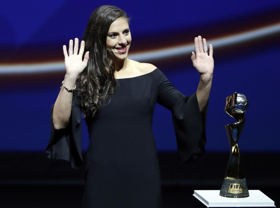 United States' Carli Lloyd waves as she stands by the World Cup trophy, during the women's soccer World Cup France 2019 draw, in Boulogne-Billancourt, outside Paris, Saturday, Dec. 8, 2018. (AP Photo/Christophe Ena)