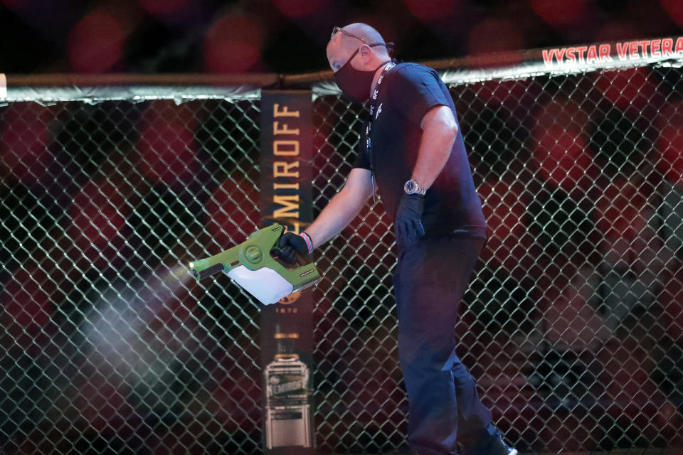 A worker sprays sanitizer in the octagon between bouts during a UFC 249 mixed martial arts competition, Saturday, May 9, 2020, in Jacksonville, Fla. (AP Photo/John Raoux)