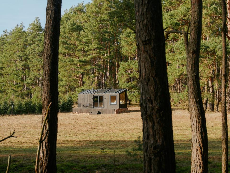 A Raus cabin in nature surrounded by tall trees and open fields.