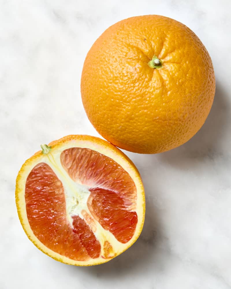 overhead shot of one whole and one half cara cara orange on a white marble surface.