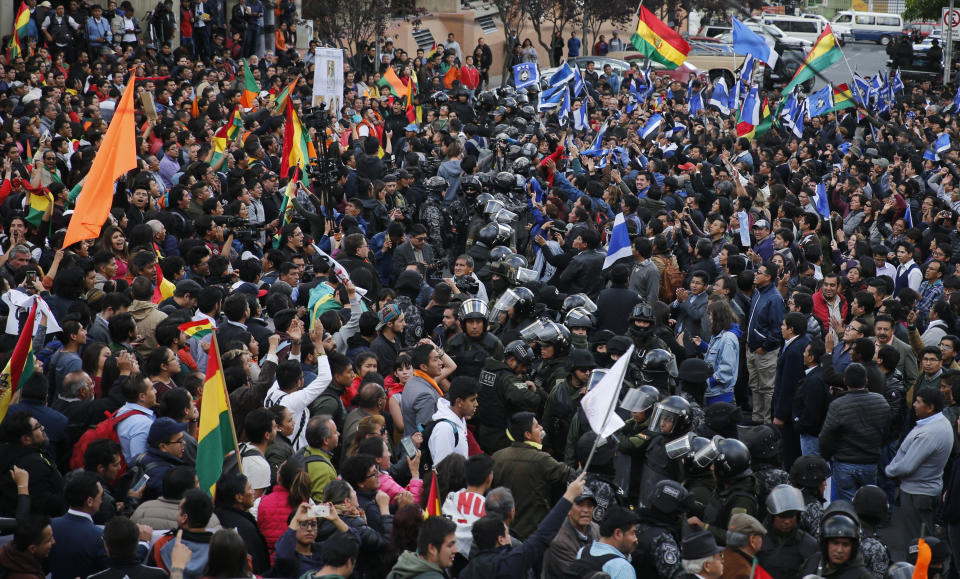 A line of police separate supporters of opposition presidential candidate Carlos Mesa, a former president, left, from supporters of Bolivian President Evo Morales, who is running for his fourth term, outside the Supreme Electoral Court where election ballots are being counted in La Paz, Bolivia, Monday, Oct. 21, 2019. A sudden halt in release of presidential election returns led to confusion and protests in Bolivia on Monday as opponents suggested officials were trying to help Morales avoid a risky runoff. (AP Photo/Jorge Saenz)