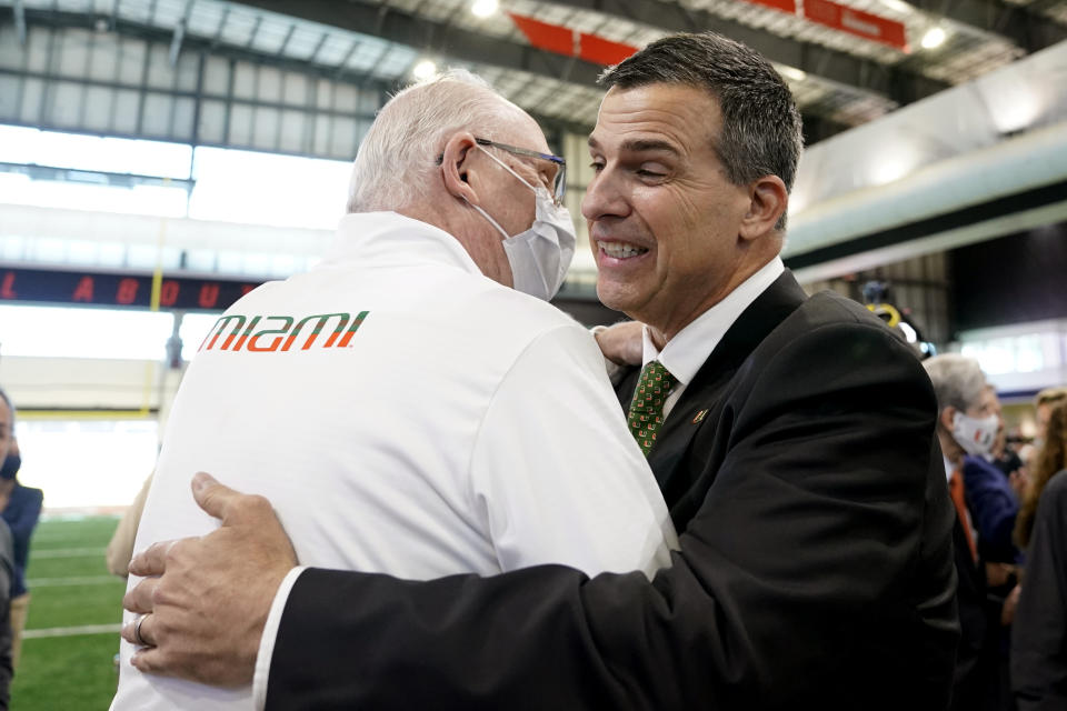 Miami's new football coach, Mario Cristobal, right, is embraced by Miami men's basketball coach Jim Larranaga, left, after being introduced at a news conference Tuesday, Dec. 7, 2021, in Coral Gables, Fla. Cristobal is returning to his alma mater, where he won two championships as a player. (AP Photo/Lynne Sladky)