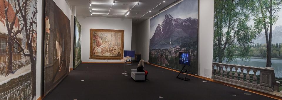 A woman watches a video presentation surrounded by soundstage and set paintings at the new exhibition "Art of the Hollywood Backdrop" at the Boca Raton Museum of Art in Boca Raton, Fla., on Friday, April 22, 2022.