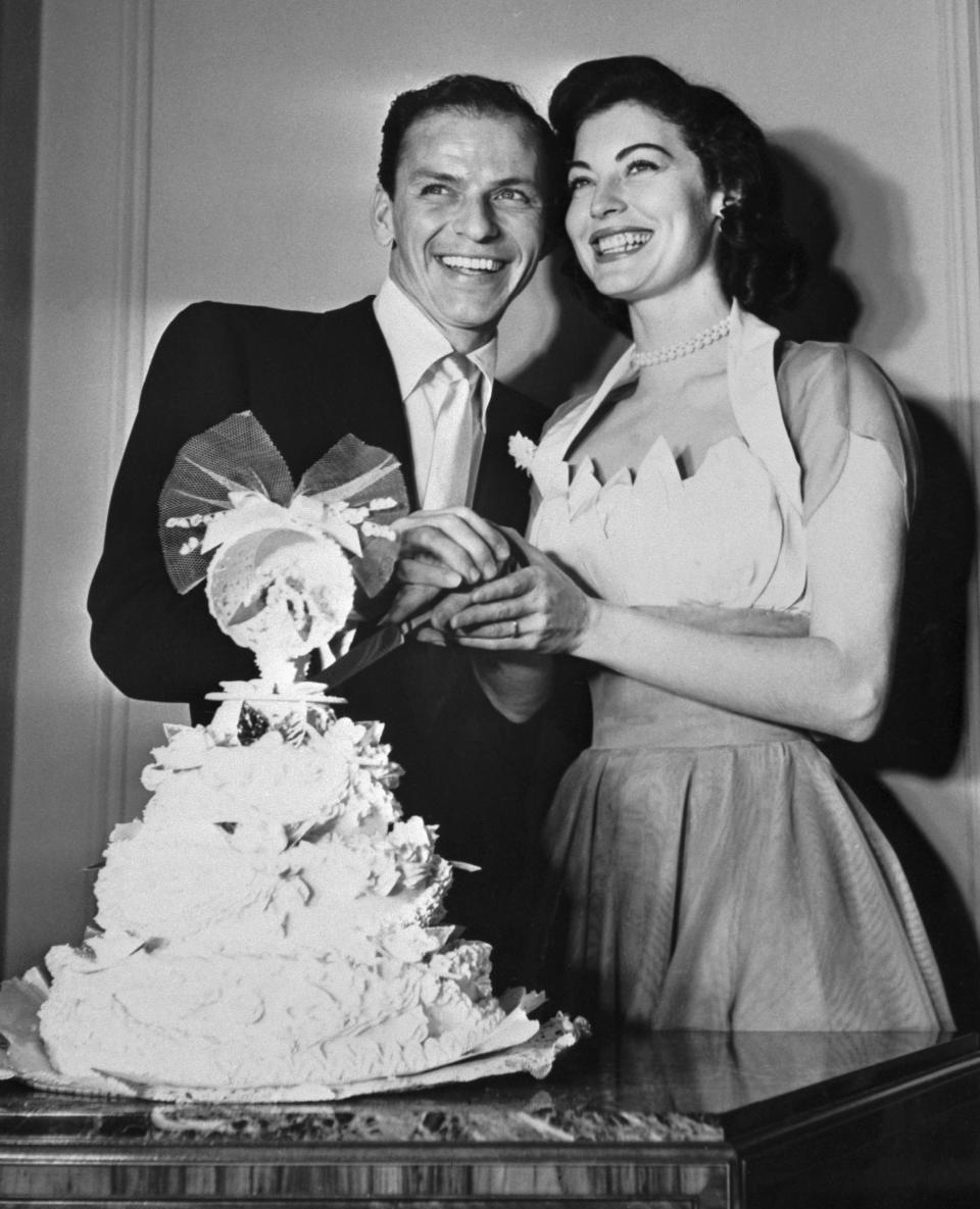 Frank Sinatra and Ava Gardner clasp hands to cut the wedding cake.