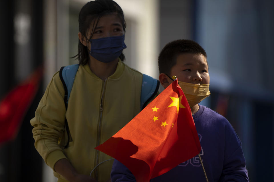 FILE - A boy wearing a face mask carries a Chinese flag as he walks along a pedestrian shopping street in Beijing on Oct. 6, 2022. China has announced its first overall population decline in recent years amid an aging society and plunging birthrate. (AP Photo/Mark Schiefelbein, File)