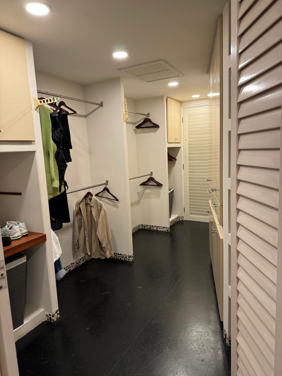 A spacious walk-in closet with neatly organized clothing hangers, shelves, and several hanging garments, including a trench coat and green top