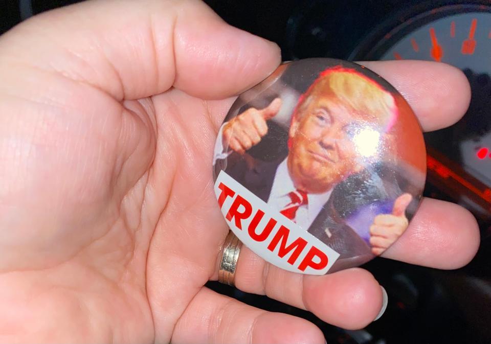Woman holding button with Donald Trump giving two thumbs up on it
