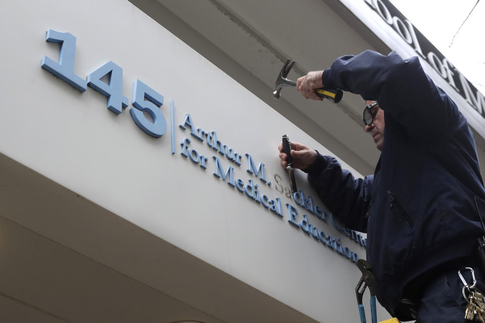 Worker Gabe Ryan removes a sign that includes the name Arthur M. Sackler at an entrance to Tufts School of Medicine, Thursday, Dec. 5, 2019, in Boston. Tufts University says it is stripping the Sackler name from its campus in recognition of the family's connection to the opioid crisis. (AP Photo/Steven Senne)