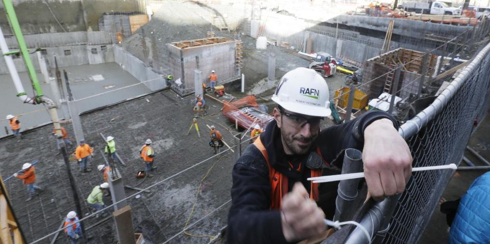 A worker straps down cloth covering a construction fence at a Seattle construction site, Wednesday, Feb. 12, 2014, where what is believed to be an ice age mammoth tusk was discovered on Tuesday. Work pouring cement at the site was continuing, but workers blocked off the area where the tusk was found. Paleontologists from the University of Washington hope to move the tusk to a museum on campus. (AP Photo/Ted S. Warren)