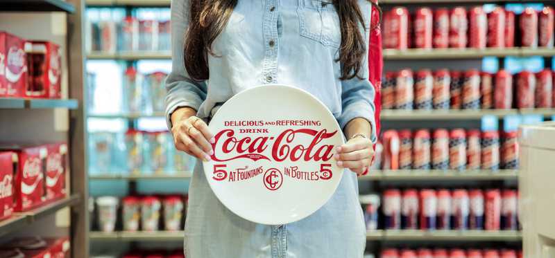 Woman holding a coca-cola plate inside a coke store.