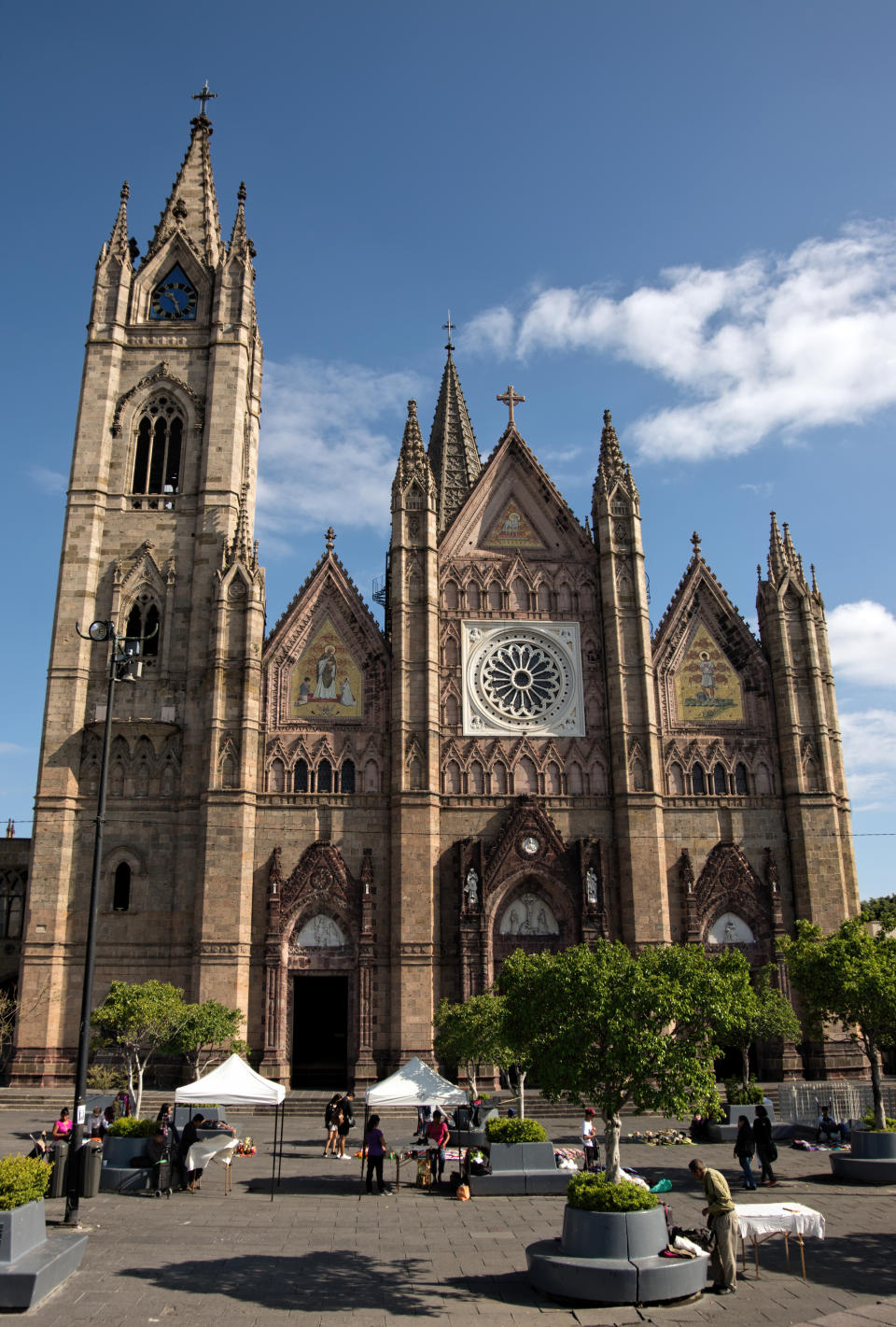 Guadalajara, Jalisco, Mexico - September 22, 2019: In the foreground, people can be seen at outdoor market stalls in Parque Expiatorio in front of the Church of the Atonement (Templo Expiatorio del Sant&#xed;simo Sacramento). The church was built in the neo-gothic architecture style over the course of 75 years (1897-1972).