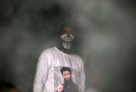 A man wearing a T-shirt with an image of Zakir Rashid Bhat also known as Zakir Musa, the leader of an al Qaeda affiliated militant group in Kashmir, as smoke billows from a room of a residential house that was damaged during a gun battle between Zakir and Indian security forces, in Dadasara village in south Kashmir's Tral May 24, 2019. REUTERS/Danish Ismail