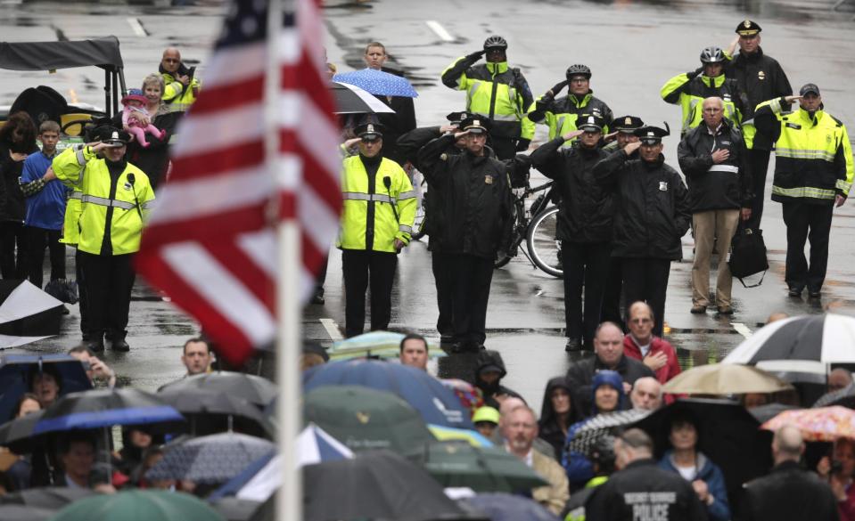 Varios policías saludan mientras se iza la bandera estadounidense en la línea de meta durante una ceremonia para conmemorar el primer aniversario de los atentados al Maratón de Bostón, el martes 15 de abril de 2014 en esa ciudad. (Foto AP/Charles Krupa)