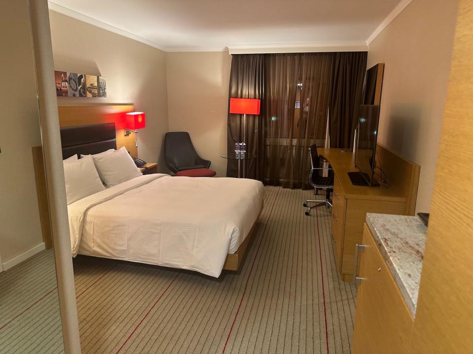hotel room with bed tv countertop red lamps and black armchair on striped tan carpeting