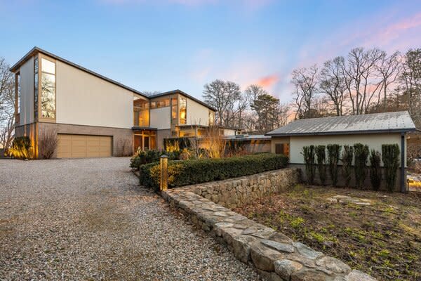 A stone-bordered driveway leads to the home, which sits nestled among soaring trees.