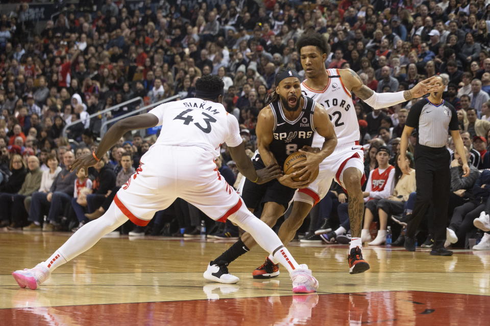 San Antonio Spurs' Patty Mills, center, drives between Toronto Raptors' Pascal Siakam and Patrick McCaw during first-half NBA basketball game action in Toronto, Sunday, Jan. 12, 2020. (Chris Young/The Canadian Press via AP)