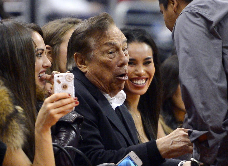 In this photo taken on Friday, Oct. 25, 2013, Los Angeles Clippers owner Donald Sterling, center, and V. Stiviano, right, watch the Clippers play the Sacramento Kings during the first half of an NBA basketball game, in Los Angeles. The NBA is investigating a report of an audio recording in which a man purported to be Sterling makes racist remarks while speaking to his Stiviano. NBA spokesman Mike Bass said in a statement Saturday, April 26, 2014, that the league is in the process of authenticating the validity of the recording posted on TMZ's website. Bass called the comments "disturbing and offensive." (AP Photo/Mark J. Terrill)