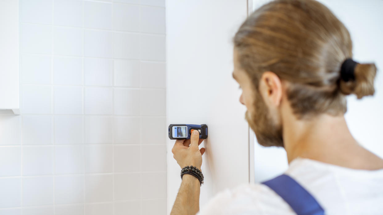  Man holding one of the best laser measures against a bathroom wall 