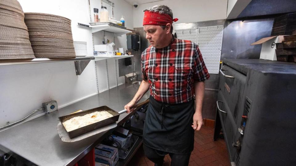 Matty Evans, chef of Rise Up! Pizza, pulls a partially completed Detroit-style pizza from the oven. The pizza is made with cheese directly on the doughy crust.