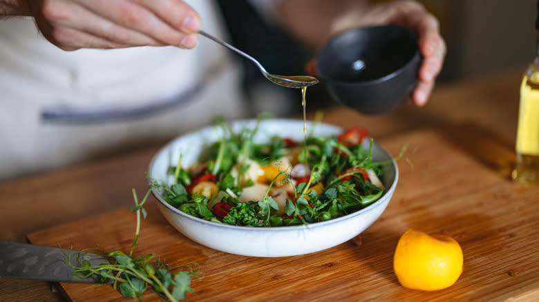 person spooning dressing over salad