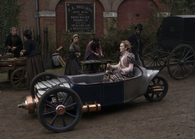 A Victorian woman drives a three-wheeled sports car