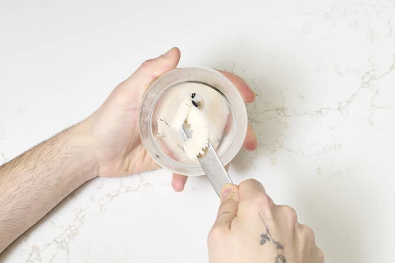 overhead shot of wax being scraped out of the candle jar with a knife.