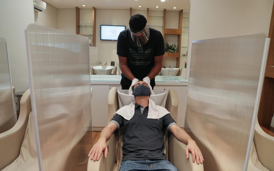 A hairdresser wearing protective mask and face shield dries customer's hair between acrylic walls set up for social distancing - AMANDA PEROBELLI/Reuters