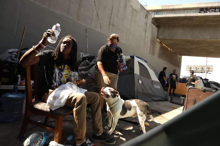 LOS ANGELES, CA - JULY 08, 2020 - - Los Angeles Homeless Services Authority (LAHSA) outreach worker Monica Palma, center, visits with Kim M. and her dog Dee-O-G who live homeless under the Santa Monica freeway along Venice Blvd. in Los Angeles on July 8, 2020. Victor Hinderliter, background, right, associate director with Los Angeles Homeless Services Authority (LAHSA), and LAHSA outreach worker Brandon Rincon, third from right, visit with Jesse James Taylor, 50, at his encampment. The city and county of Los Angeles plan to move people from the freeways. U.S. District Judge David O. Carter passed a landmark court order banning homeless encampments from under and along Los Angeles freeways. (Genaro Molina / Los Angeles Times)