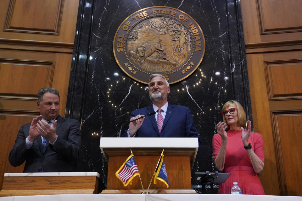 Indiana Gov. Eric Holcomb, middle, prepares to deliver his State of the State address to a joint session of the legislature at the Statehouse, Tuesday, Jan. 10, 2023, in Indianapolis. House Speaker Todd Huston, R-Fishers, is at left and Lt. Gov. Suzanne Crouch, applauds during the introduction. (AP Photo/Darron Cummings)