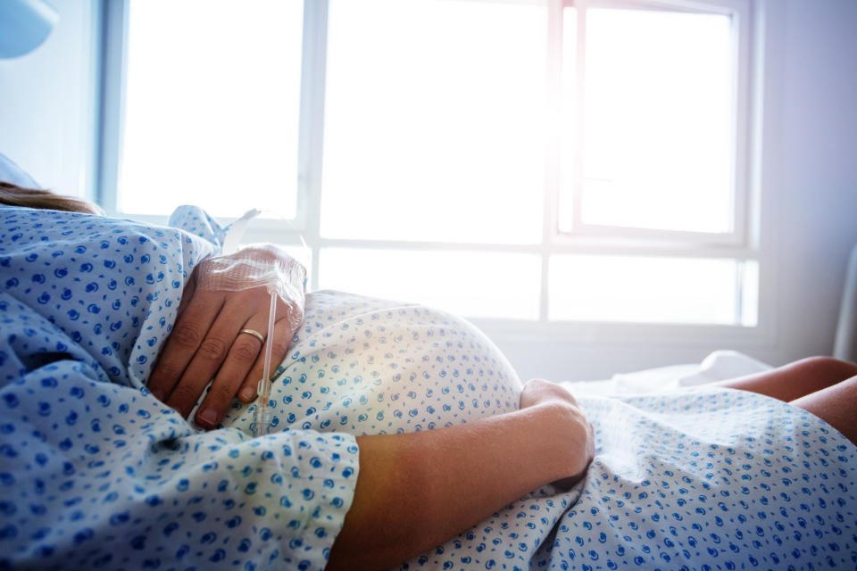 Pregnant woman lying in a hospital bed, wearing a hospital gown, with a window in the background