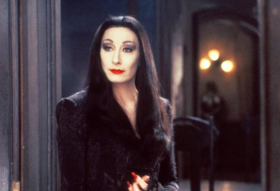 Morticia Addams from "The Addams Family" stands solemnly, dressed in her signature long black dress