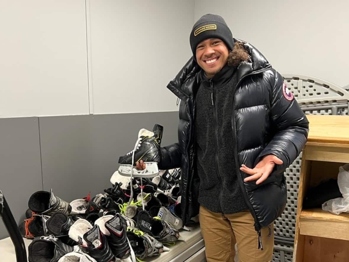 Elladj Baldé poses with dozens of pairs of figure skates, which he and the Skate Global Foundation donated to the Temple community in Calgary. (Submitted by Michelle Dawley - image credit)