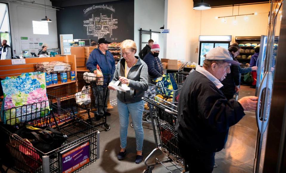 Volunteer Tammy Ambrose (center) of Lake Tapps keeps shelves stocked as shoppers move through the Sumner Community Food Bank in Sumner, Washington, on Wednesday, May 18, 2022.