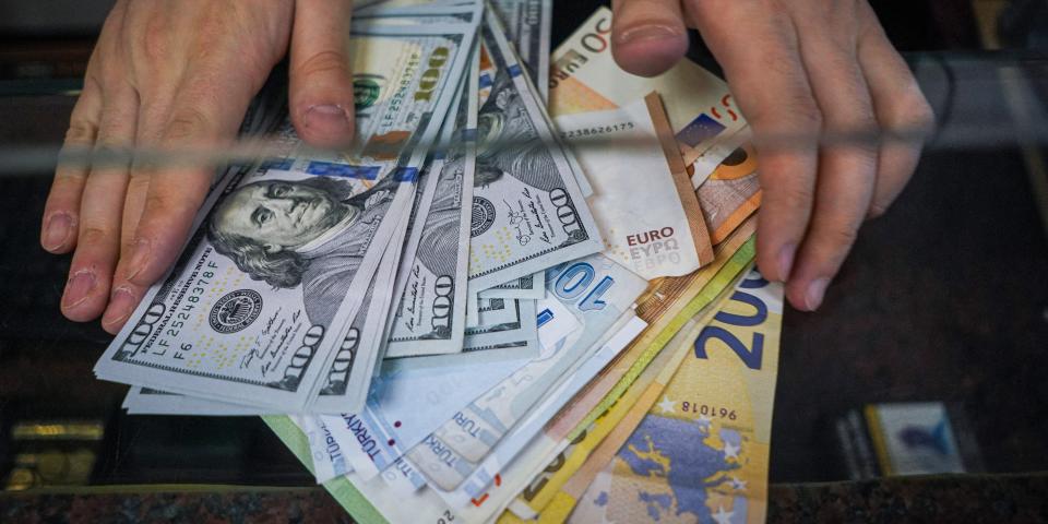 A man's hands hold dollar, euro and Turkish lira bills in a foreign exchange office.