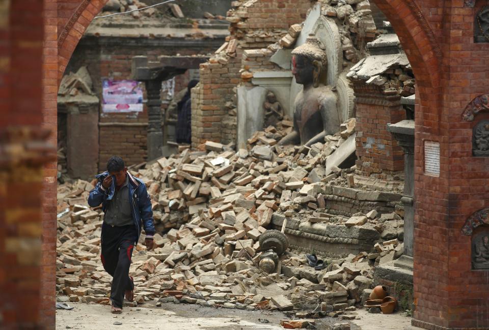 A man cries as he walks on the street while passing through a damaged statue of Lord Buddha. (Reuters)