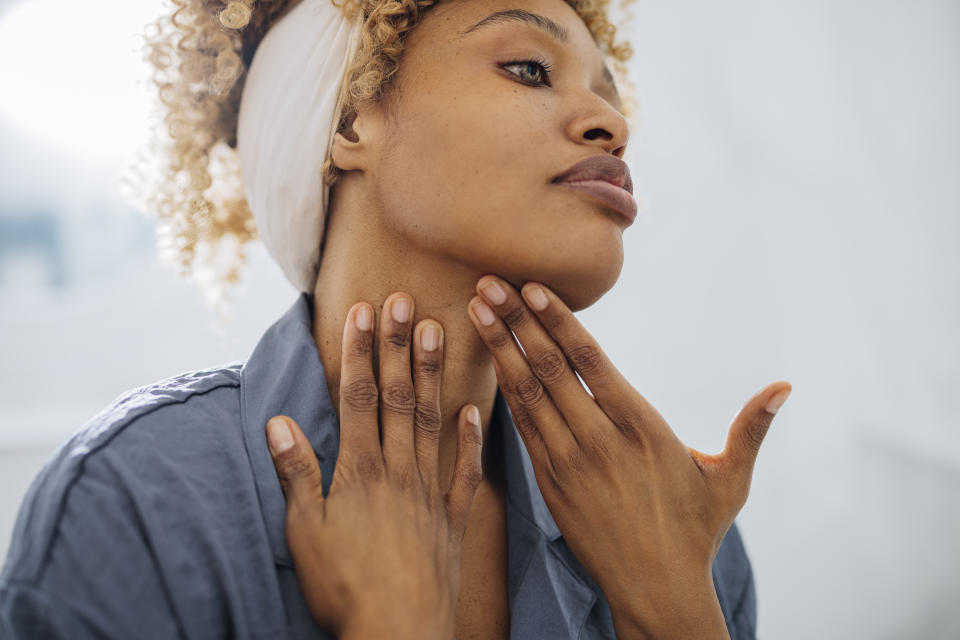 Beautiful woman looking away and touching her neck with her hands. She is standing in her bathroom. She is probably putting face cream on her neck.