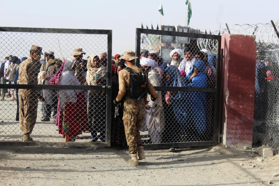 A Pakistani soldier holds a gate as Afghan and Pakistani people wait to enter Afghanistan through the Pakistan-Afghanistan border crossing point in Chaman (AFP via Getty Images)