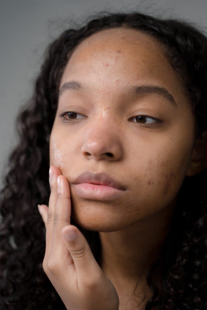 Black woman examining her face in the mirror.