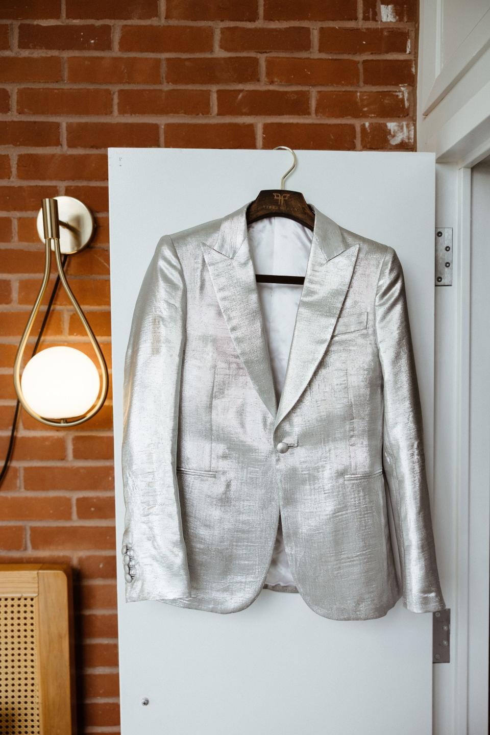 A silver jacket hangs on a door in front of a brick wall.