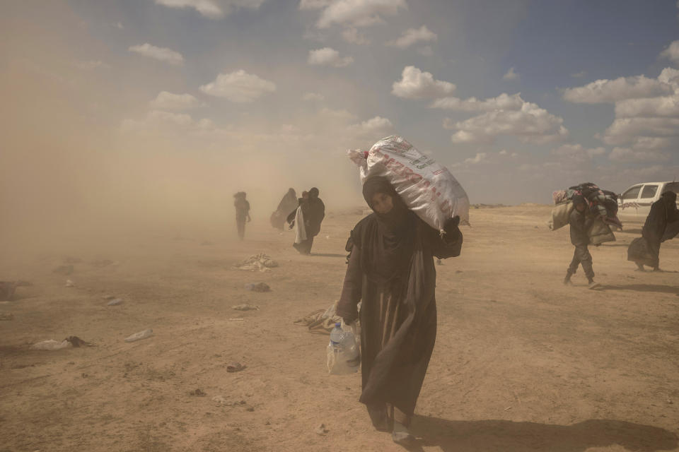 In this Wednesday, March 6, 2019, photo, a woman carries supplies from a reception area for people evacuated from the last shred of territory held by Islamic State militants, outside Baghouz, Syria. (AP Photo/Gabriel Chaim)