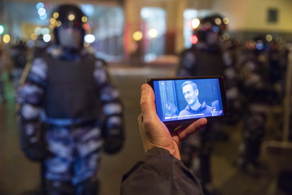 FILE In this file photo taken on Tuesday, Feb. 2, 2021, A journalist watches a live stream of a court hearings with the Russian opposition leader Alexei Navalny on a screen as Russian Rosguardia (National Guard) soldiers guard in front of the court in Moscow, Russia. The January protests in scores of cities across the sprawling country were the largest outpouring of discontent in years and appeared to have rattled the Kremlin. Police reportedly arrested about 10,000 people in the protests and many demonstrators were beaten, while state media sought to downplay the scale of the protests. (AP Photo/Pavel Golovkin, File)