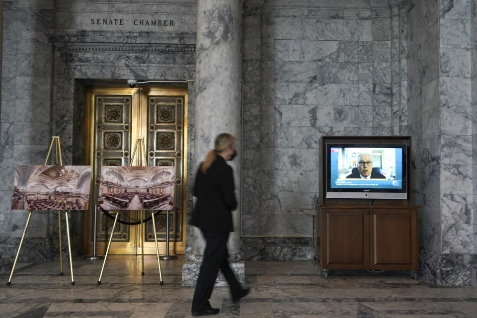 A Senate security worker walks near a video display outside the Senate chamber showing Washington Gov. Jay Inslee testifying remotely at a committee hearing on a bill that would make it a gross misdemeanor for elected officials or candidates to knowingly lie about election outcomes if those claims result in violence, Friday, Jan. 28, 2022, at the Capitol in Olympia, Wash. (AP Photo/Ted S. Warren)