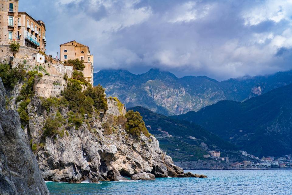 Atrani is one of the most remote destinations that was used as a filming location for the series "Ripley". 
pictured: a rocky coast of Atrani, Italy with mountains surrounding the background