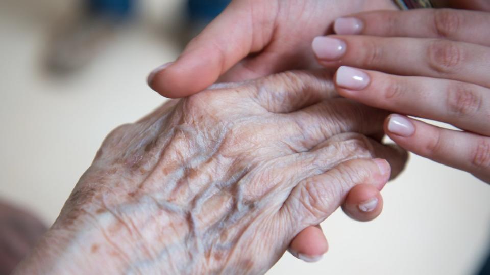 Eine Pflegerin hält die Hand einer älteren Dame. Foto: Christophe Gateau