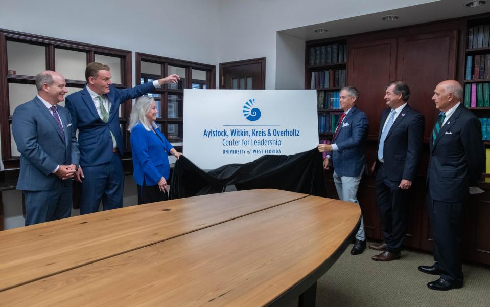 UWF President Martha Saunders, center left, and attorney Justin Witkin unveil a sign for the Aylstock, Witkin, Kreis & Overholtz Center for Leadership at the University of West Florida in recognition of a $2.5 million donation from the law firm during a press conference in downtown Pensacola on Tuesday.