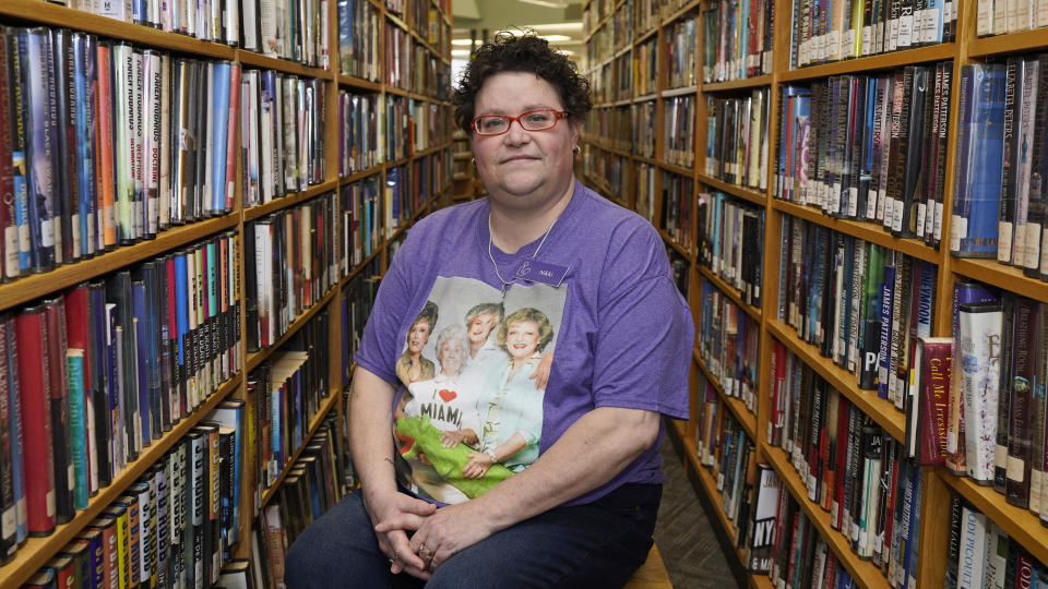 Nikki Luman, who works part-time for a local library, poses between books, Monday, March 8, 2021, in Sycamore, Ohio. Roughly 4 in 10 Americans say they're still feeling the financial impact of the loss of a job or income within their household as the economic recovery remains uneven one year into the coronavirus pandemic. A new poll by The Associated Press-NORC Center for Public Affairs Research provides further evidence that the pandemic has been devastating for some Americans, while leaving others virtually unscathed or even in better shape, at least when it comes to their finances. The outcome often depended on the type of job a person had and their income level before the pandemic. (AP Photo/Tony Dejak)