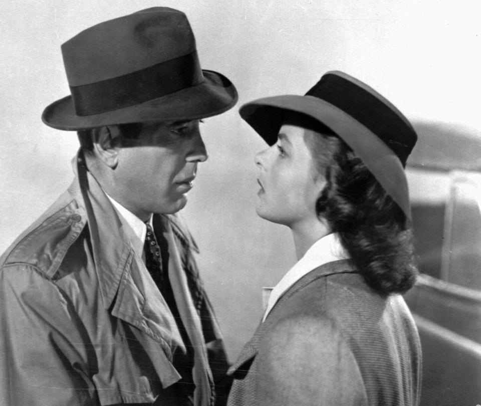 A black-and-white movie still of a man and a woman, both in hats, looking into each other's faces
