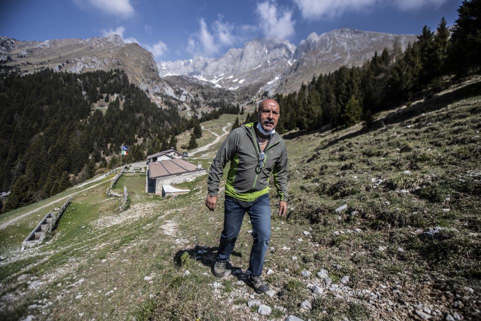 In this image take on Friday, April 24, 2020 Claudio Trentani, 57, walks outside his shelter 'Baita Cassinelli', at 1568mt, at the foot of Mt. Presolana, seen in the background, in Castione della Presolana, near Bergamo, northern Italy. Of the COVID-19 pandemic he says, “It is a powerful tragedy that has touched chords that not even during the war had been touched.” (AP Photo/Luca Bruno),