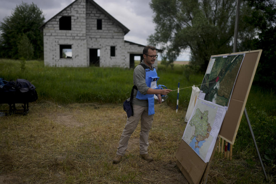 A mine detection worker with the HALO Trust de-mining NGO explains how they search for anti-tank and anti personnel land mines in Lypivka, on the outskirts of Kyiv, Ukraine, Tuesday, June 14, 2022. Russia’s invasion of Ukraine is spreading a deadly litter of mines, bombs and other explosive devices that will endanger civilian lives and limbs long after the fighting stop. (AP Photo/Natacha Pisarenko)